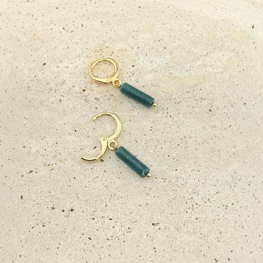 A pair of Aking Sinta gold huggie hoop earrings with dark green African jade column drops. One earring is unlatched to show the hinge mechanism, photographed on a natural light-colored stone background.