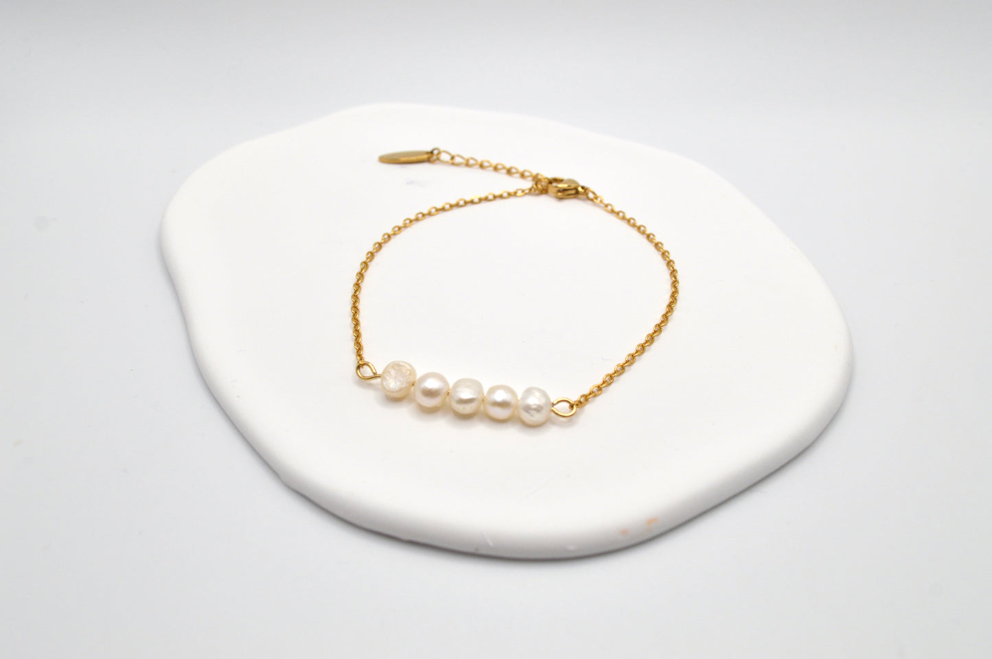 Aking Sinta gold chain bracelet with five Baroque pearls resting on a large, iridescent white Mother of Pearl shell display.
