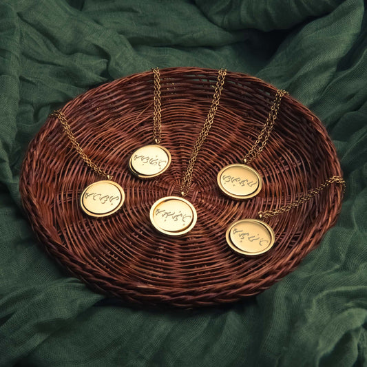 A collection of five gold Aking Sinta spinning coin fidget necklaces arranged in a woven wicker basket. Each circular pendant is custom-engraved with ancient Filipino Baybayin script. The necklaces feature delicate gold chains and are styled against a textured dark green fabric backdrop