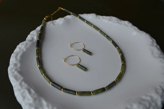 A pair of gold hoop earrings with vertical Canadian Jade column charms resting inside a shimmering Mother of Pearl shell container; the dark green translucent stones contrast beautifully with the iridescent pink and white background.