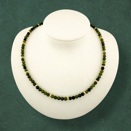 A minimalist Aking Sinta Canadian Jade beaded necklace displayed on a white bust; featuring a continuous strand of opaque, deep forest-green gemstones accented with small polished gold beads; no hanging charm or extender chain.