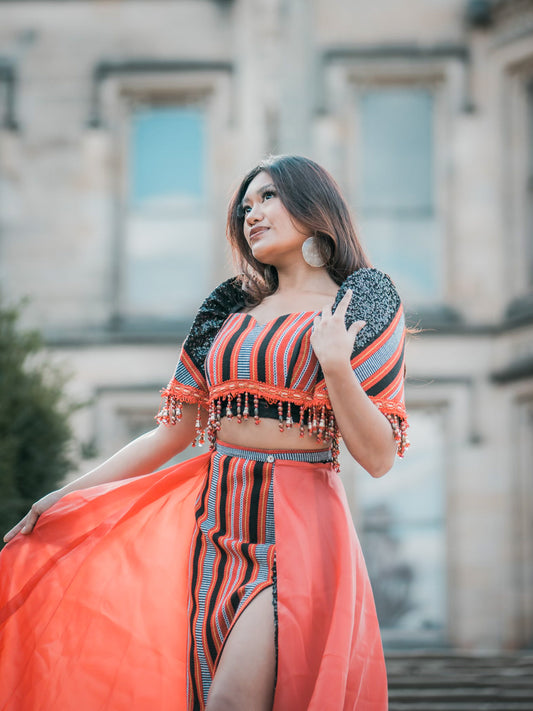 A side-profile view of a woman wearing a traditional Ifugao woven tribal dress in deep red and black earthy tones, accessorized with large Aking Sinta Gold Lined Capiz Shell Earrings; the oversized iridescent disks glow against the intricate patterns of the hand-loomed fabric.
