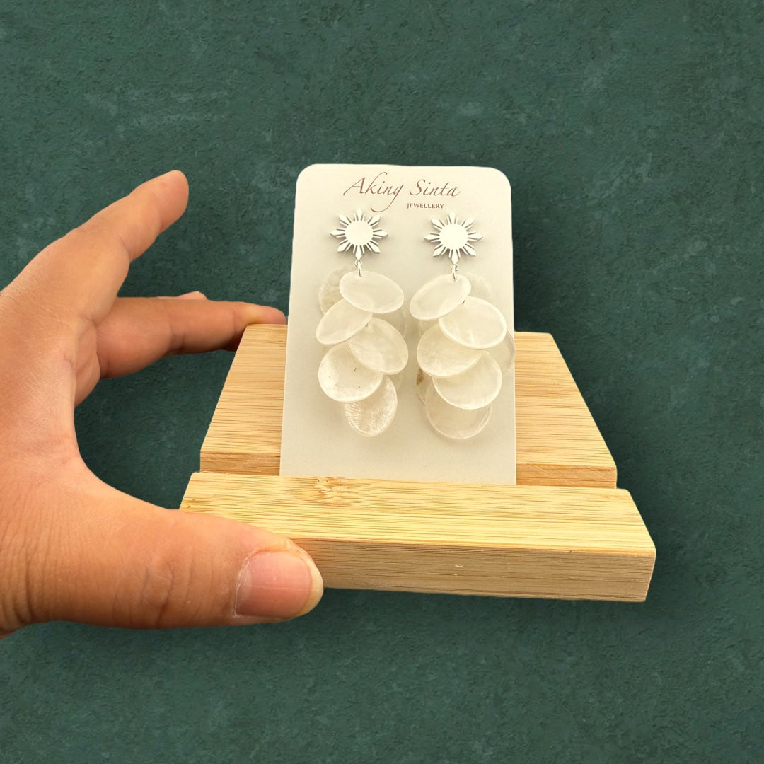 Aking Sinta Cascading Capiz Shell Araw Stud Earrings silver variant displayed on branded cardboard holder placed on wooden stand, highlighting lightweight design and Philippine-inspired craftsmanship