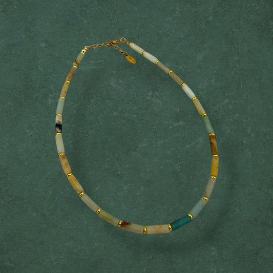 Aking Sinta Flower Amazonite necklace featuring long column-shaped beads in mint and cream, laid flat on a rich dark green background with gold bead accents.