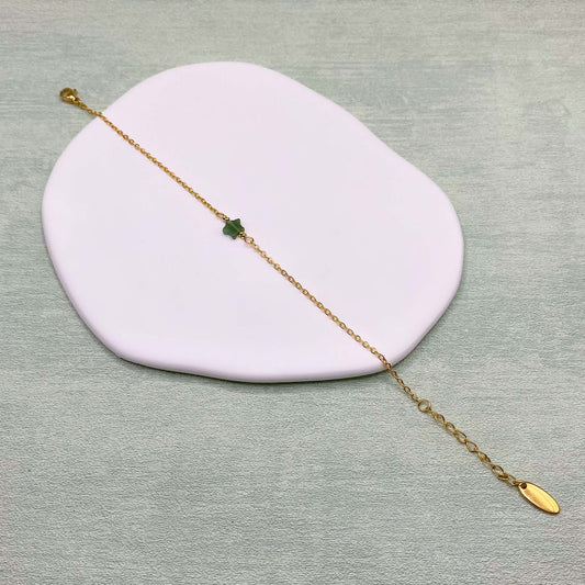 An Aking Sinta product photograph showing the dainty green aventurine star bracelet laid out diagonally across an asymmetrical white display dish over a light sage green background. The delicate gold chain bracelet features a small star-shaped green aventurine gemstone charm at the center, a lobster clasp closure on one end, and an adjustable extender chain ending in an oval gold brand tag on the other