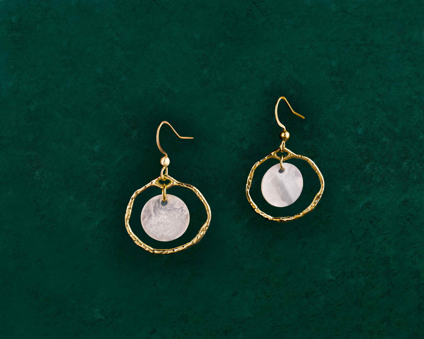 A pair of Aking Sinta gold Floating Capiz Shell Hook Earrings displayed on a dark green background; featuring thin, polished gold ear hooks with a single, round, translucent white Capiz shell disk that hangs freely.