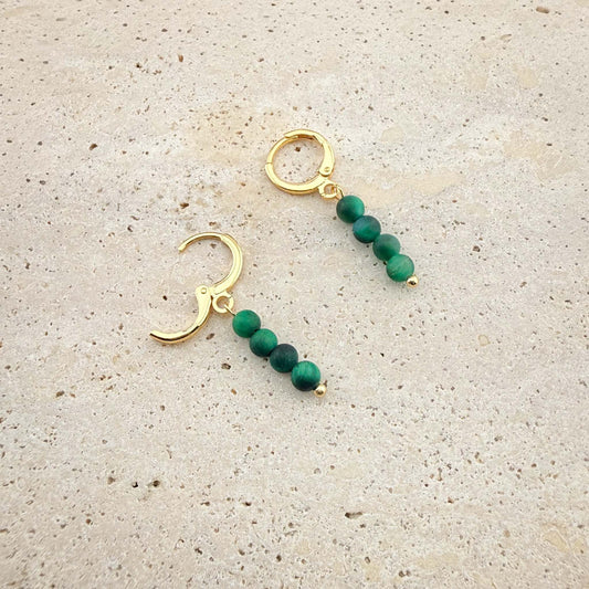 Close-up of gold Aking Sinta huggie earrings with Green Tiger Eye beads, showing one hoop closed and one hoop with the hinge clasp open on marble.
