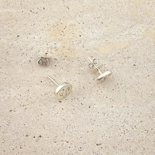 A close-up view of Aking Sinta sterling silver Lingling-O stud earrings. The image shows the butterfly scroll backs and post detail of the circular Filipino-inspired studs, displayed on a light natural stone surface