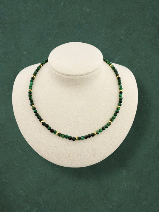 A minimalist Aking Sinta Green Tiger Eye beaded necklace on a white display holder; the strand features deep emerald-green gemstones with a silky, light-reflecting chatoyancy, accented by small polished gold beads throughout the strand; no charm or extender.