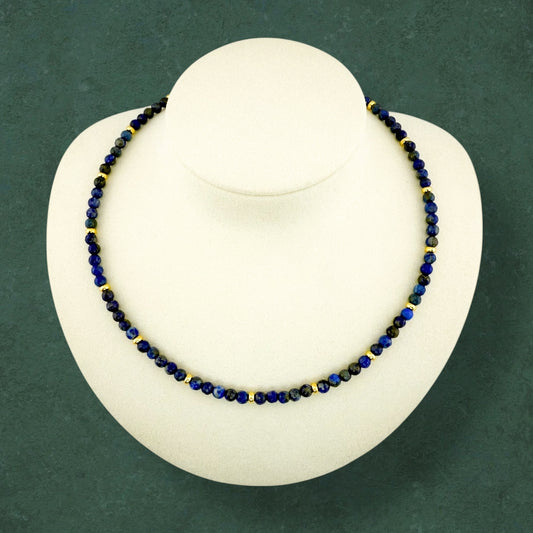 A plain Aking Sinta Lapis Lazuli beaded necklace without a charm; the deep ultramarine blue beads feature natural gold pyrite flecks, shown on a dark green background.