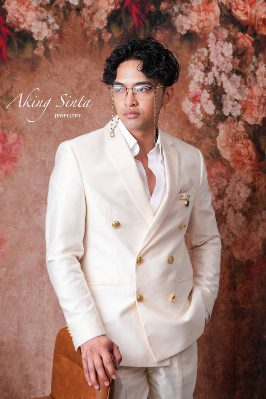Aking Sinta Safety Pin Brooch with pearl, Araw sun, and jade charms worn on left chest of model in white suit and eyeglasses, highlighting Philippine-inspired design