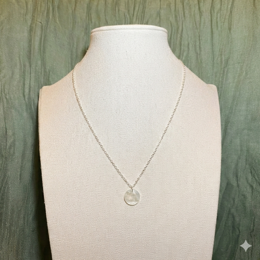 A minimalist Aking Sinta necklace featuring a single circular Capiz shell pendant on a fine silver chain; shown on a professional white display to emphasize the iridescent texture of the solo Filipino shell