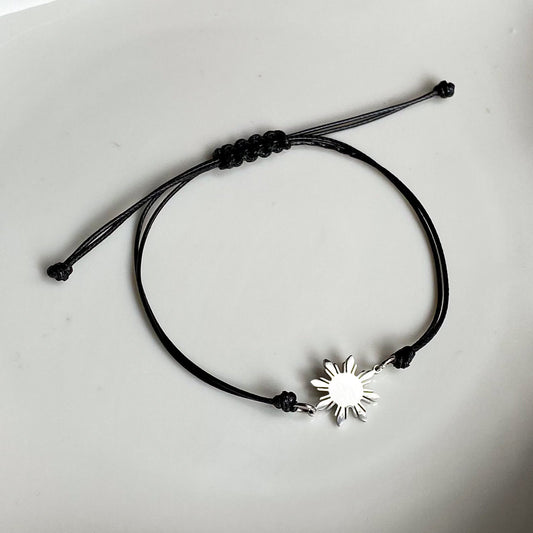 Aking Sinta unisex friendship bracelet featuring a polished silver 8-ray Philippine sun charm on a durable black cord; displayed on a white background to emphasize the sharp contrast and modern design.
