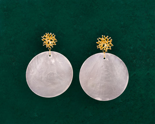A detailed close-up of a pair of Aking Sinta Statement Capiz and Coral Stud earrings on a dark green background; featuring large, round white Capiz shell disks with a small, round, bright red coral stone fixed at the center of each.