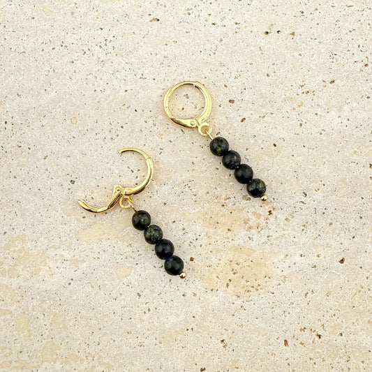 A pair of gold huggie earrings with three-bead Serpentine drops on a textured white rock background; one gold clasp is open to show the hinge, while the other is snapped shut, highlighting the light green translucent beads.