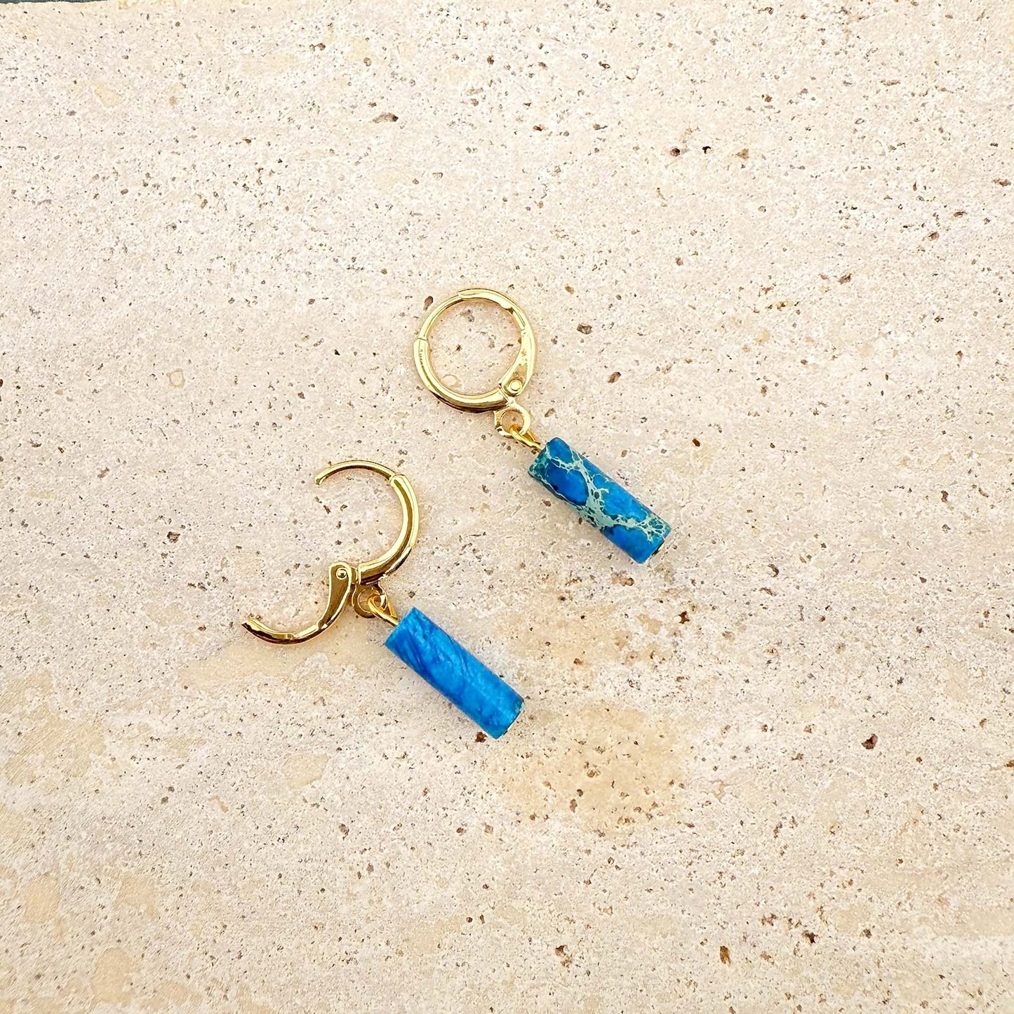 Gold circular ocean blue Imperial Jasper earrings on marble, showing one huggie clasp open to reveal the hinge and post.