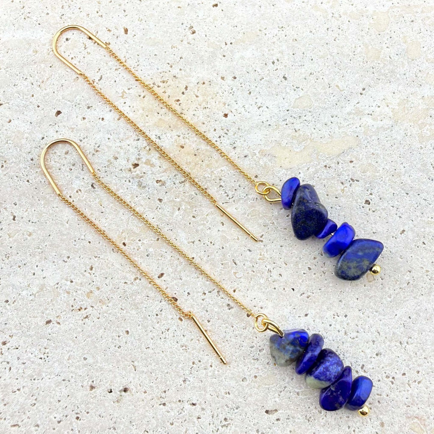 Long 18K gold-plated threader earrings featuring raw Lapis Lazuli nugget charms on a white marble texture.