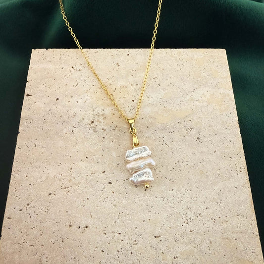 Wide view of a gold dainty necklace with three spaced flat Keshi pearls resting on a large white marble surface.