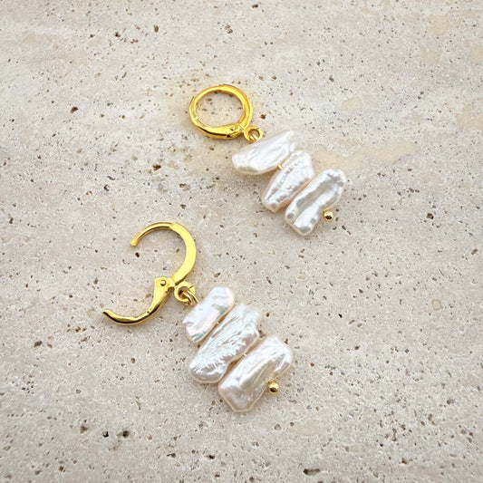 Close-up of gold Triple Flat Keshi Pearl earrings on marble, showing one hoop closed and one with the hinge clasp open to reveal the mechanism.