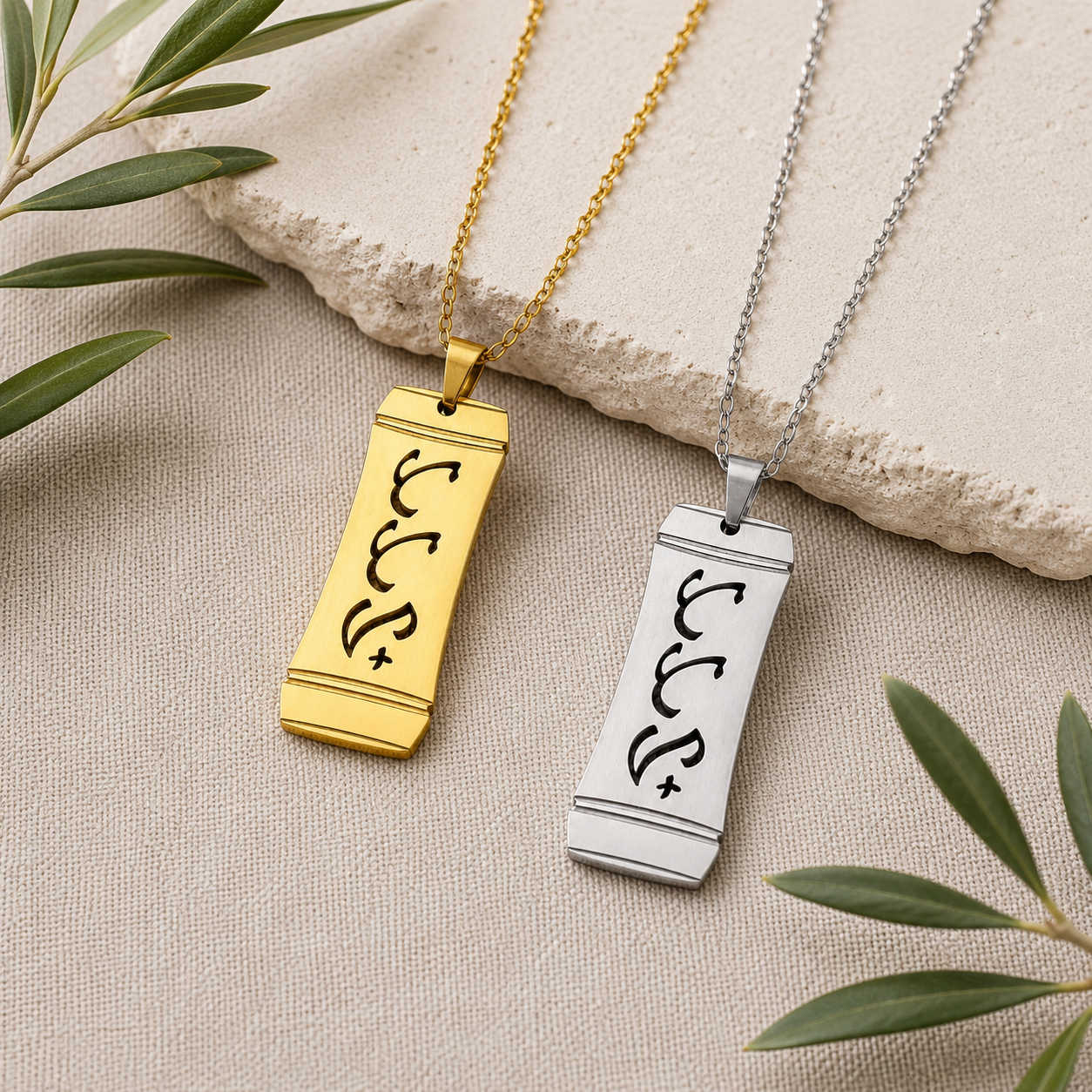 A product photograph showcasing two Aking Sinta vertical bamboo-style rectangular pendants in matte gold and silver finishes side by side. Both pendants feature the word "Tatay" (Father) intricately cut out in stylized traditional Baybayin script characters, displayed on a cream textured surface beside a light stone slab and olive leaves