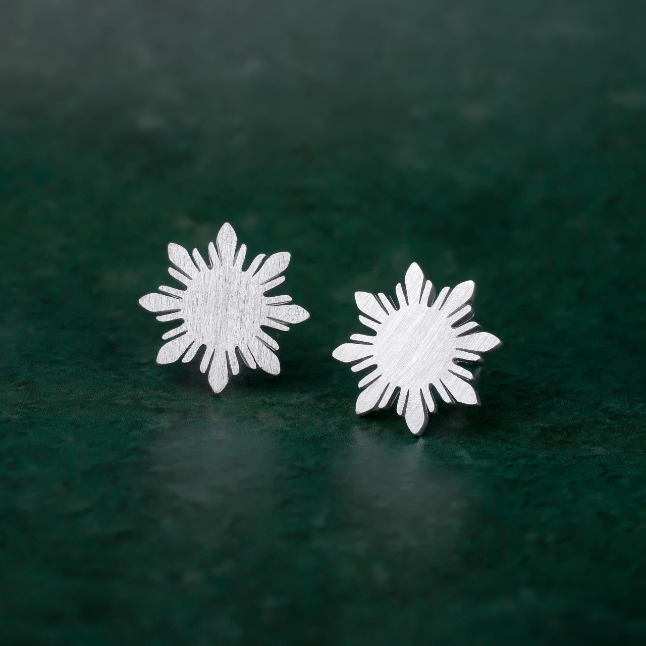 A pair of Aking Sinta Araw sterling silver stud earrings featuring the signature 8-ray sunburst design, displayed on a vibrant green background to highlight the cool-toned metallic shine