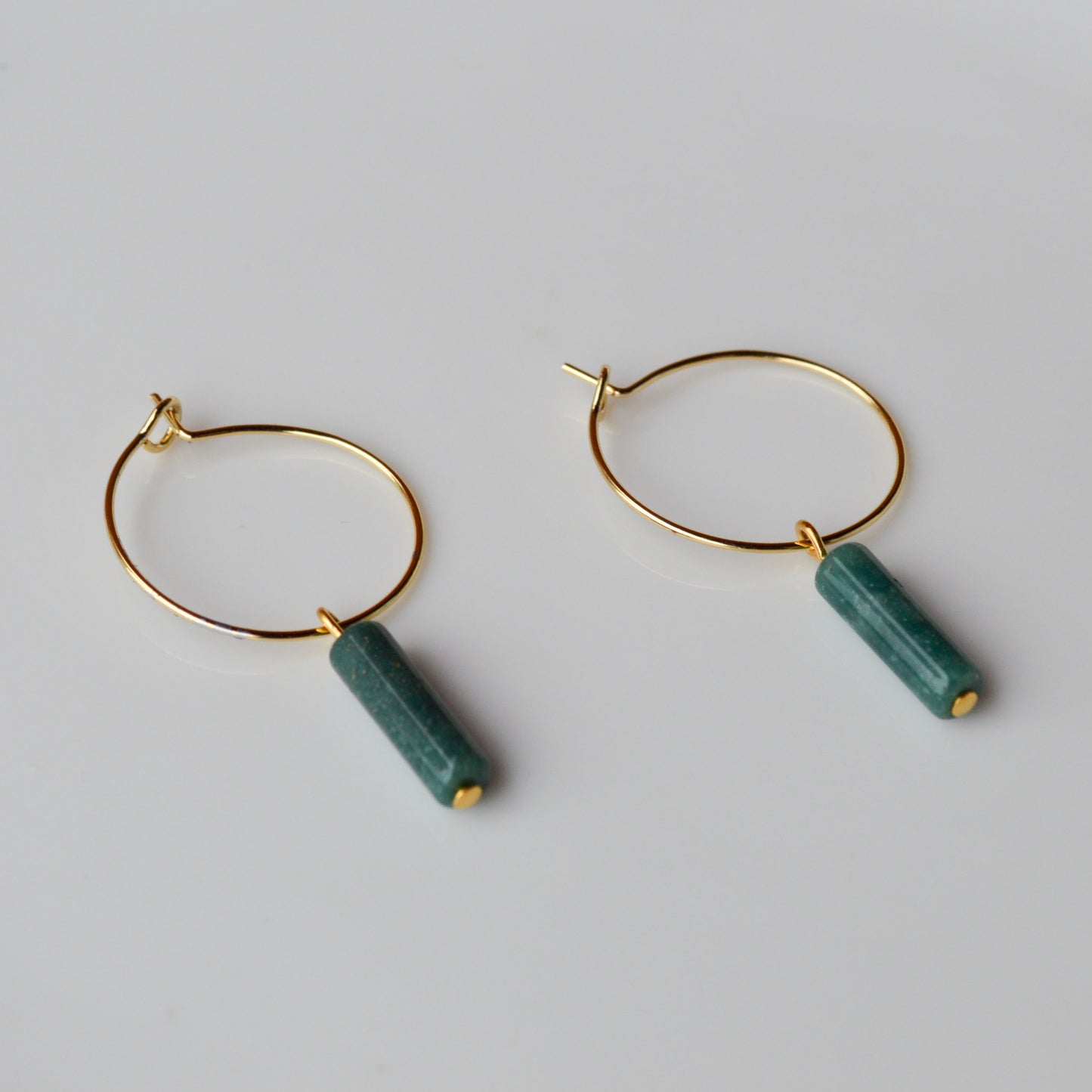 A pair of Aking Sinta gold hoop earrings on a seamless, solid white background; each hoop features a dangling, cylindrical column of African Jade in a deep, variegated moss green.