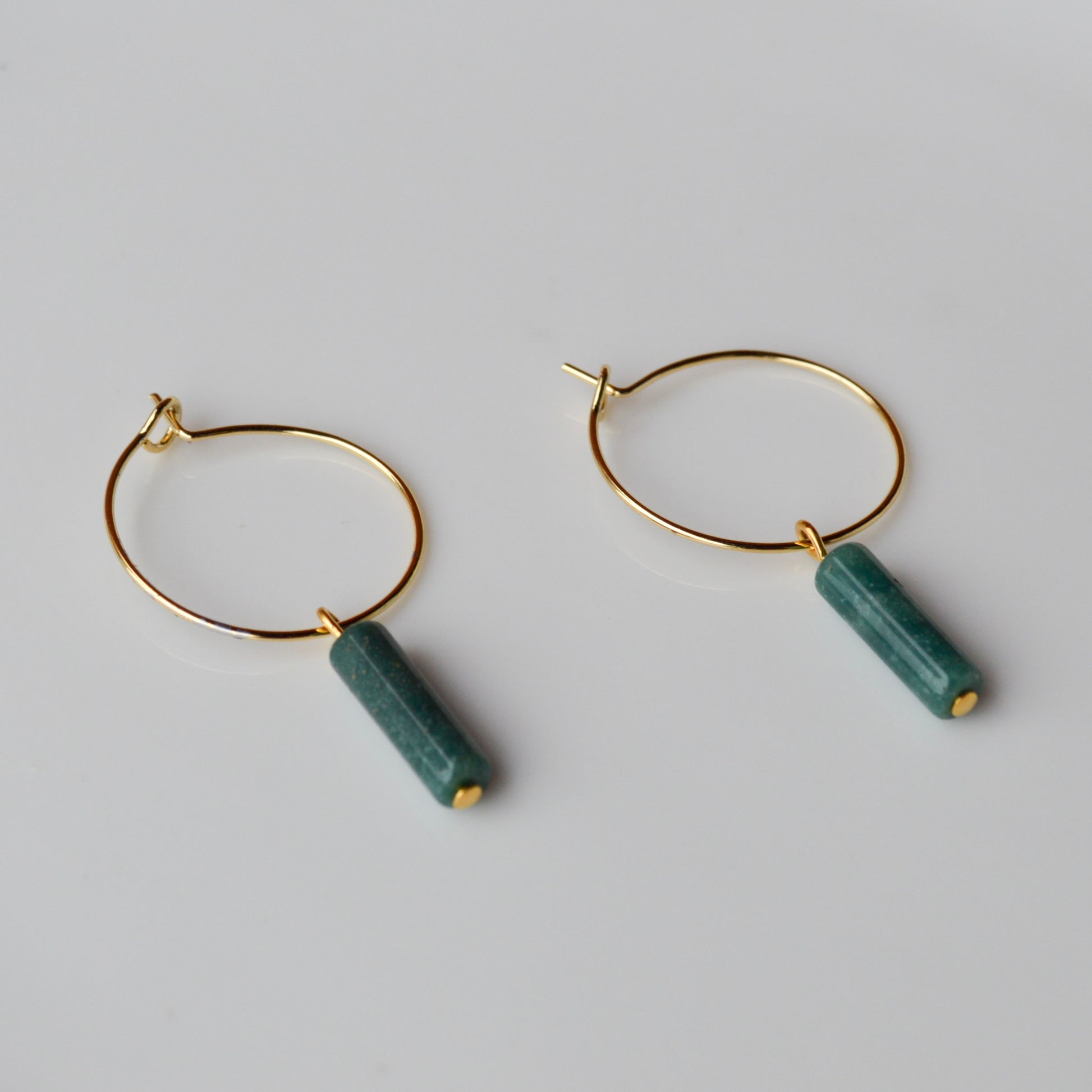 A pair of Aking Sinta gold hoop earrings on a seamless, solid white background; each hoop features a dangling, cylindrical column of African Jade in a deep, variegated moss green.