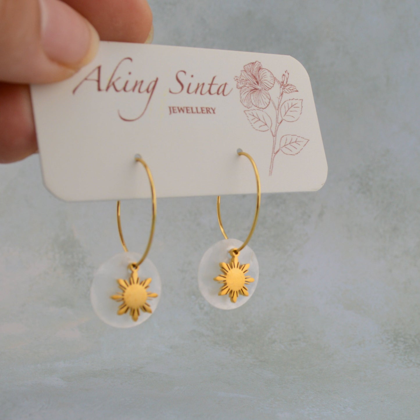 Aking Sinta Araw and Capiz Shell Dainty Hoop Earrings gold variant displayed on branded cardboard holder held by hand, highlighting lightweight design and Philippine-inspired craftsmanship