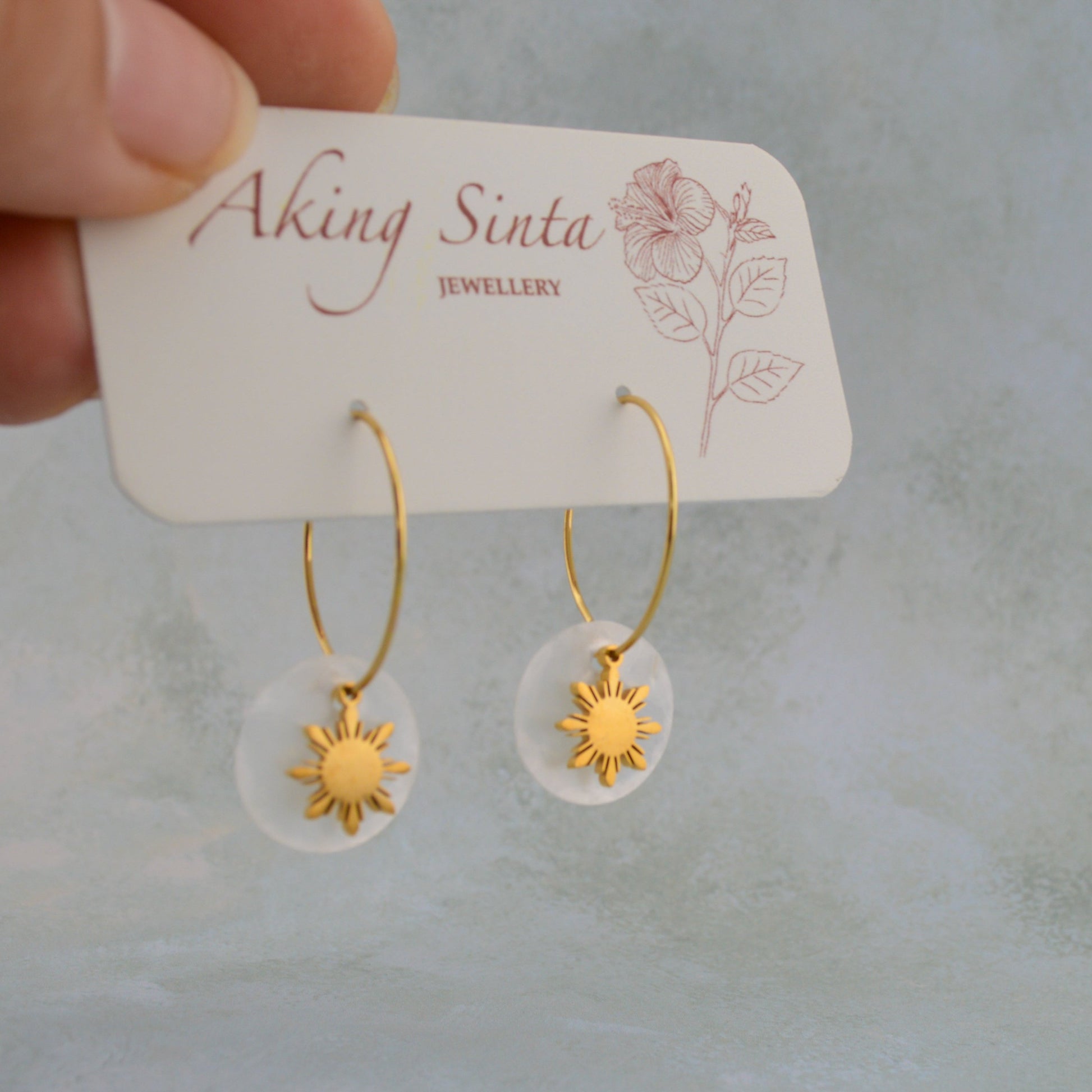 Aking Sinta Araw and Capiz Shell Dainty Hoop Earrings gold variant displayed on branded cardboard holder held by hand, highlighting lightweight design and Philippine-inspired craftsmanship