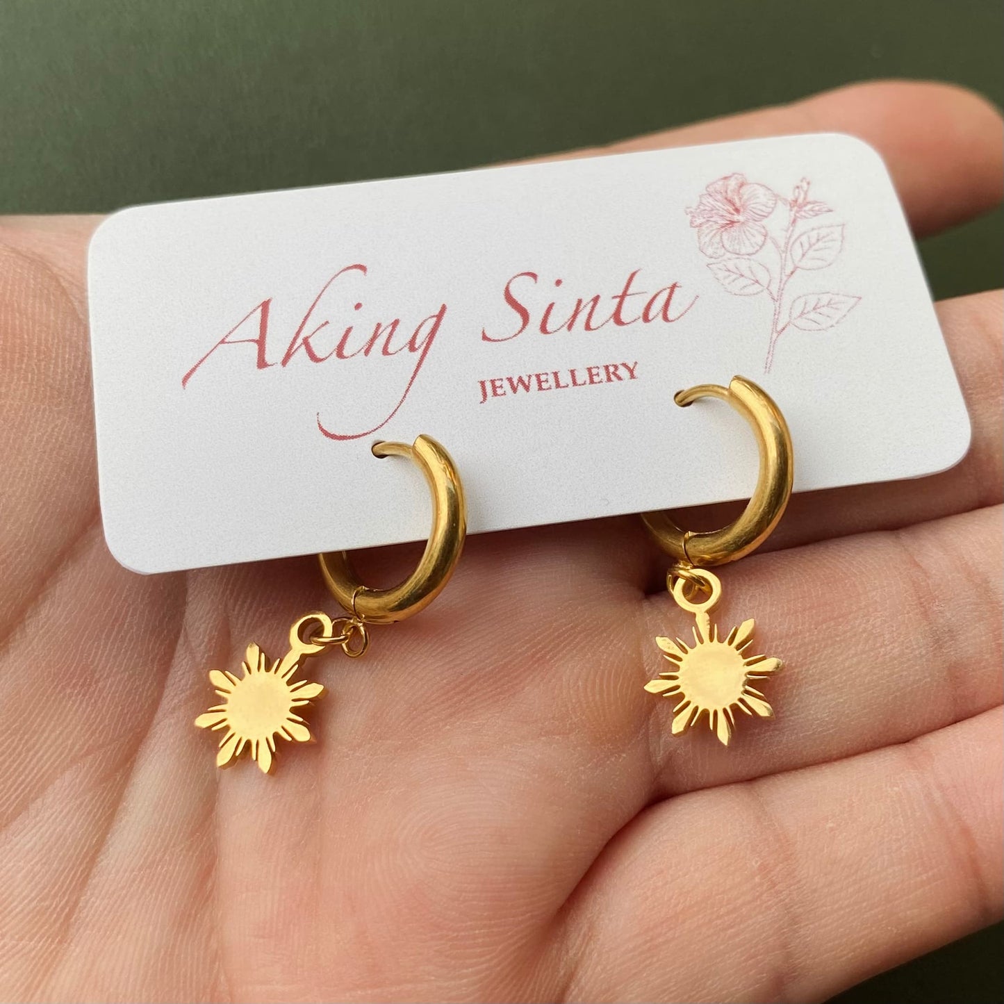 Aking Sinta Araw Charm Huggies in gold inspired by the 8-ray sun being held and placed into display pack