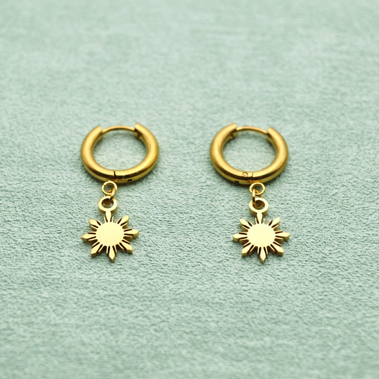 Aking Sinta Araw Charm Huggies in gold inspired by the 8-ray sun on leathery creamy background