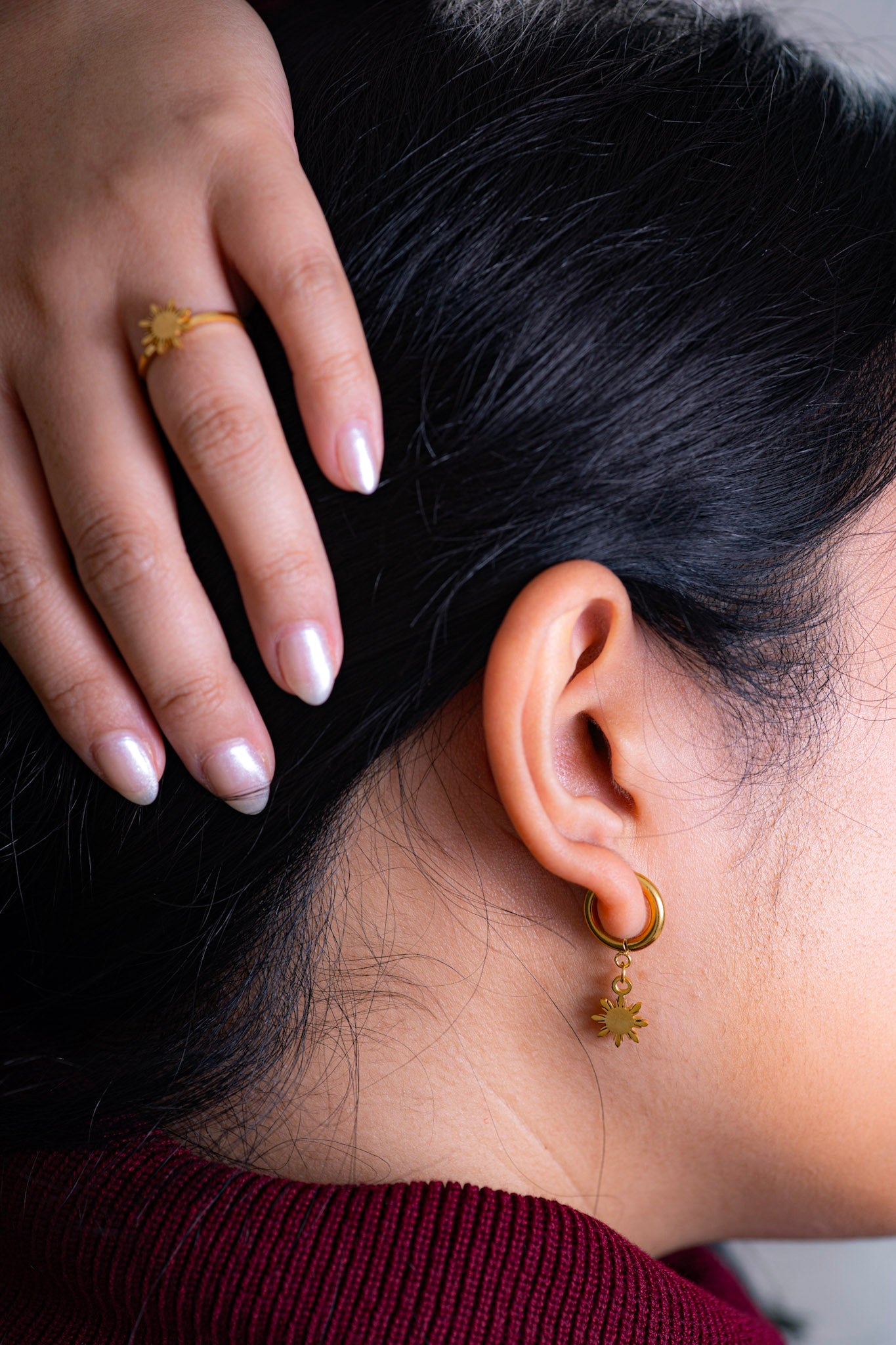 Aking Sinta Araw Charm Huggies in gold inspired by the 8-ray sun worn by woman in dark red clothing, photographed from the back with hand lifting hair to show earrings