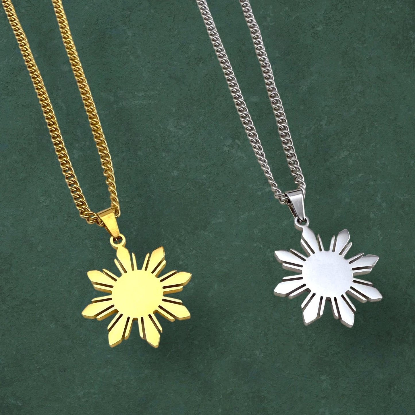 Close-up of Aking Sinta Araw Chunky Curb Chain Necklace in silver and gold variants with 8-ray sun pendant charm prominently featured on green background, highlighting bold design and Philippine-inspired craftsmanship