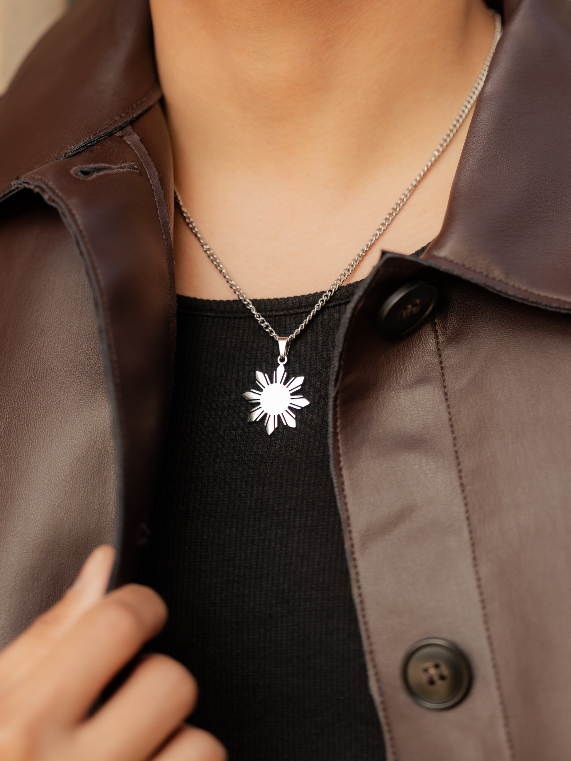 Aking Sinta Araw Chunky Curb Chain Necklace silver variant worn by man in black outfit with brown leather jacket, highlighting 8-ray sun pendant charm and bold, Philippine-inspired design