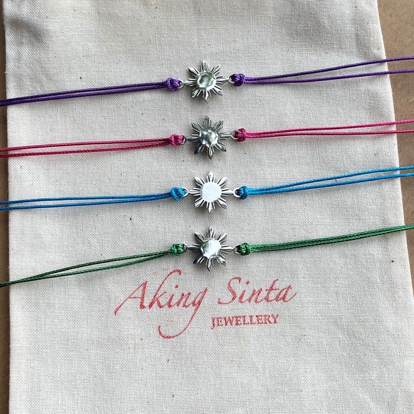 Aking Sinta Araw Friendship Bracelets in silver with blue, green, purple, and pink cords displayed on Aking Sinta jewellery pouch, Philippine-inspired jewellery for diaspora abroad