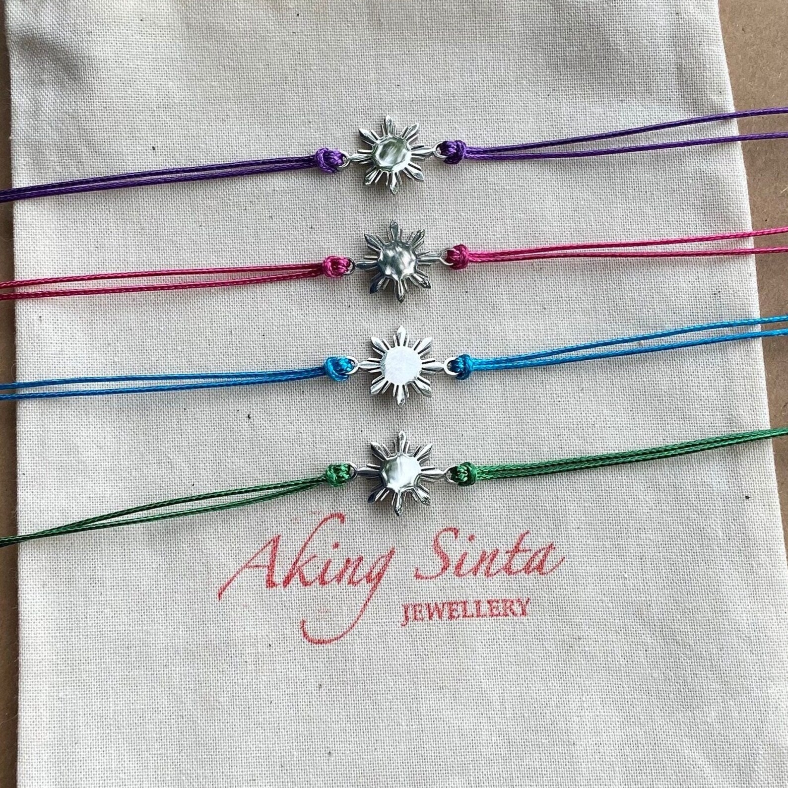 Aking Sinta Araw Friendship Bracelets in silver with blue, green, purple, and pink cords displayed on Aking Sinta jewellery pouch, Philippine-inspired jewellery for diaspora abroad