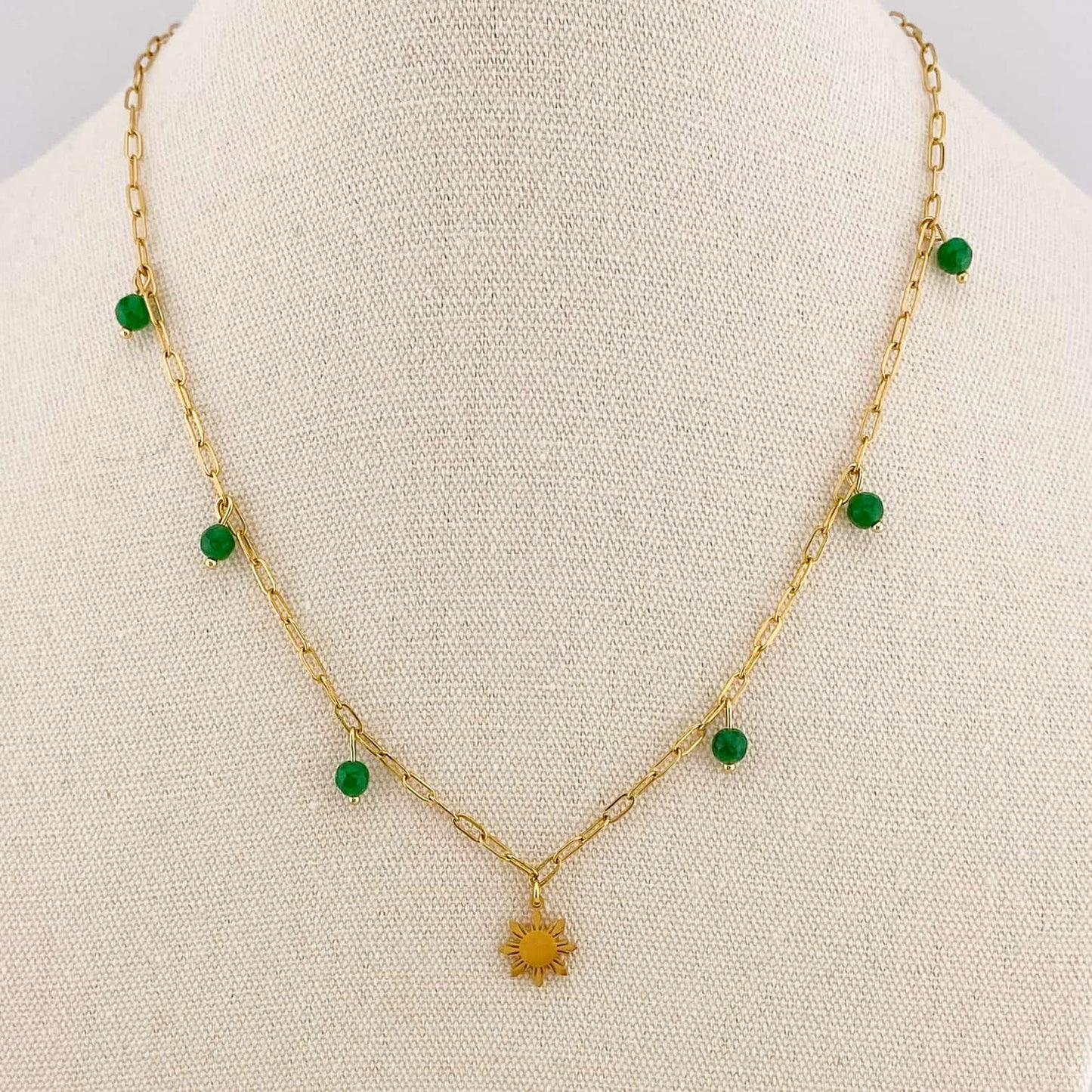 A close-up of an Aking Sinta gold paperclip necklace on a white display bust; a small green jade bead is fixed to a specific chain link, positioned alongside a detailed gold Araw sun charm.