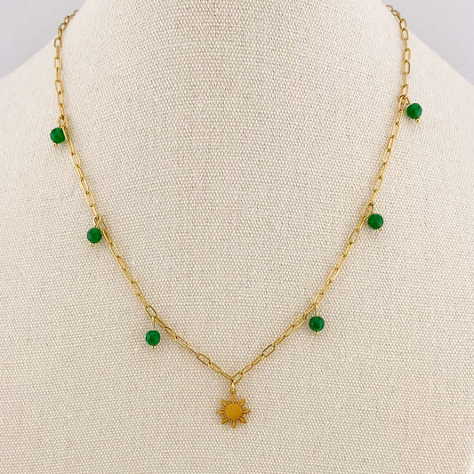 A close-up of an Aking Sinta gold paperclip necklace on a white display bust; a small green jade bead is fixed to a specific chain link, positioned alongside a detailed gold Araw sun charm.
