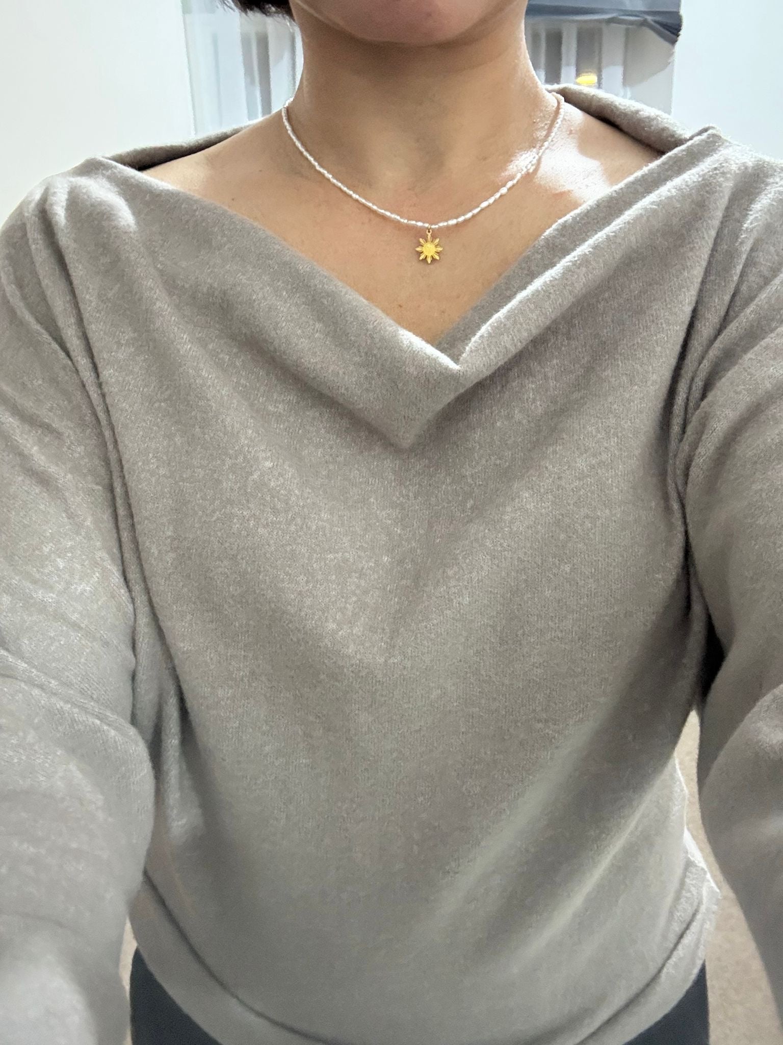 Close-up lifestyle shot of a model in a gray dress wearing the Aking Sinta Rice Pearl Necklace with a gold Philippine Sun charm; face not visible.
