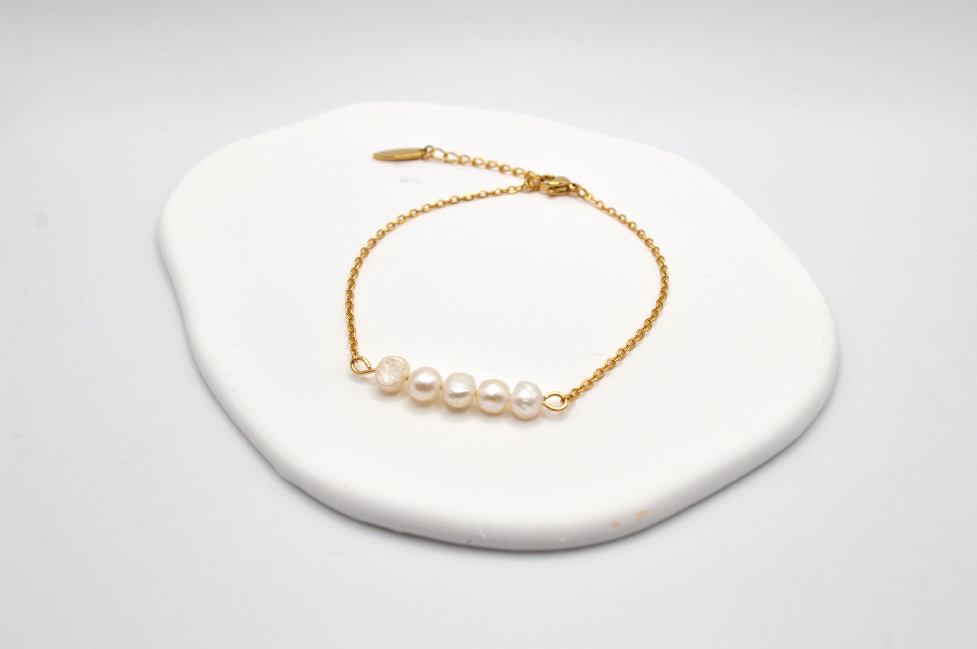 Aking Sinta gold chain bracelet with five Baroque pearls resting on a large, iridescent white Mother of Pearl shell display.