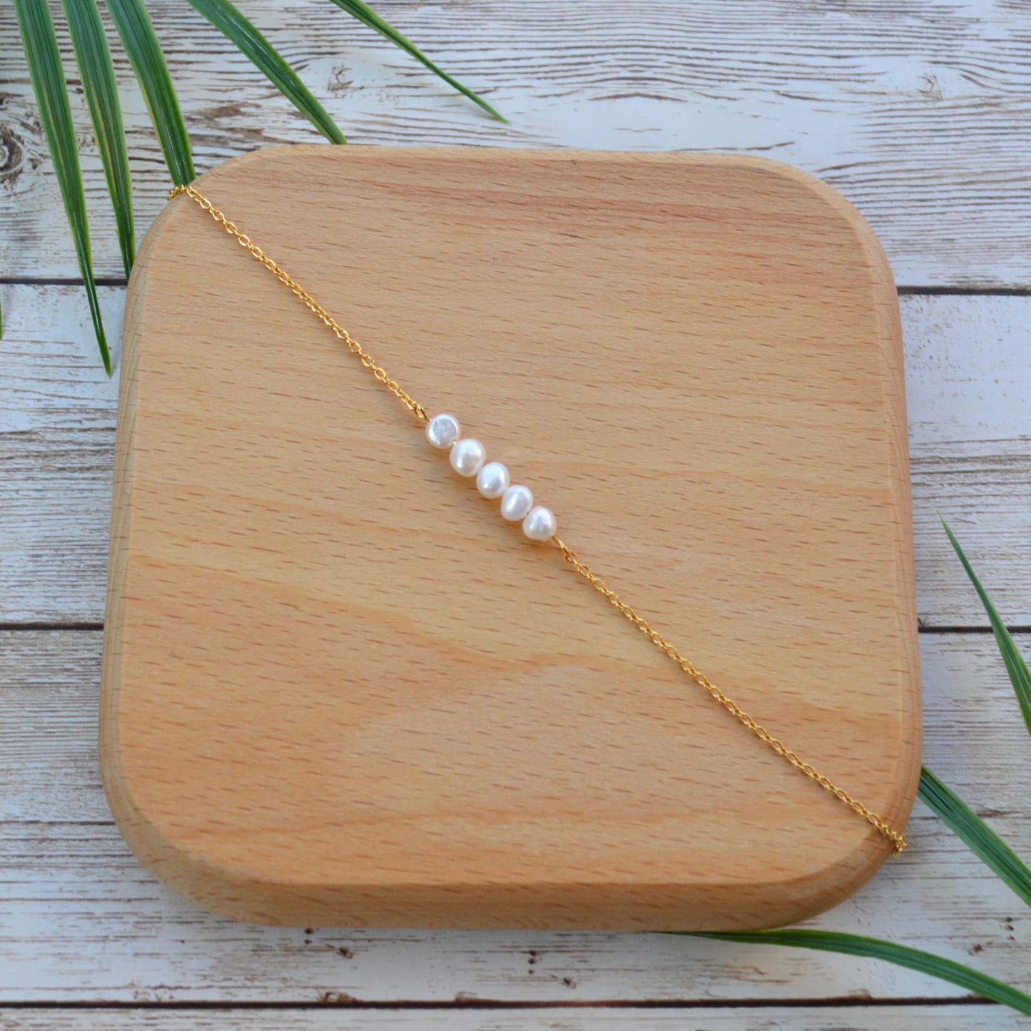 Aking Sinta gold chain bracelet with five Baroque pearls resting on a shallow wooden display plate, showing the contrast between iridescent pearls and natural wood grain.