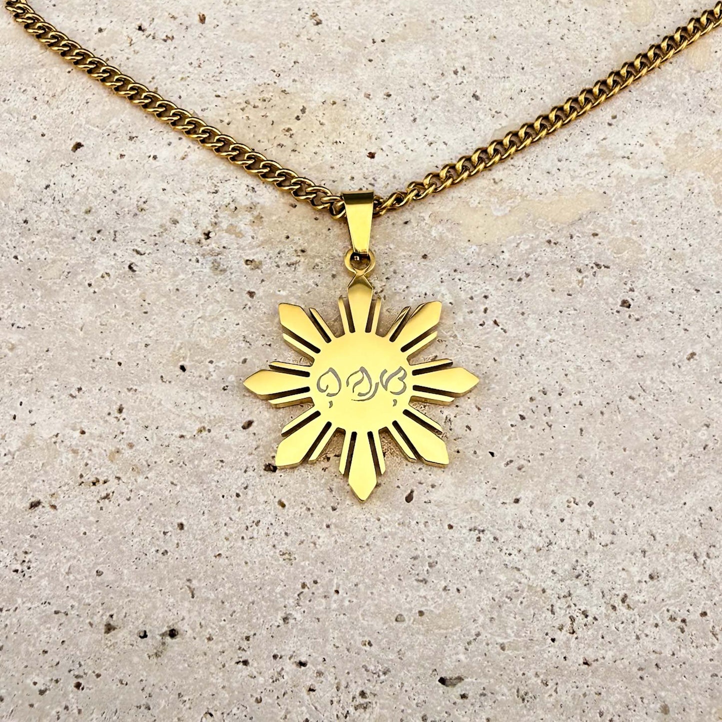 Macro close-up of a gold Aking Sinta Araw necklace featuring bespoke Baybayin script engraving, displayed on a white marble background.