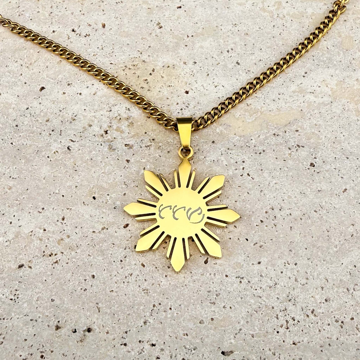 Close-up of an Aking Sinta gold Araw necklace on a marble background, featuring a third unique variant of bespoke Baybayin script engraving.