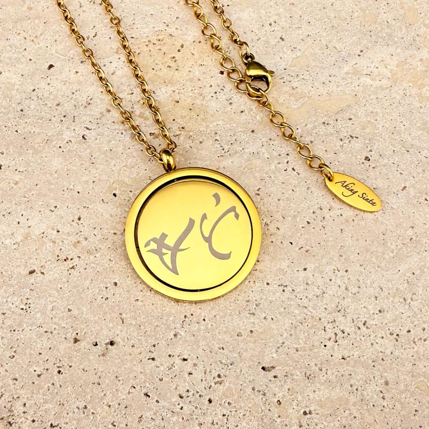 Full view of the Aking Sinta gold Spinning Coin necklace on marble, showing the bespoke Baybayin engraved coin, adjustable extender chain, and engraved brand tag.
