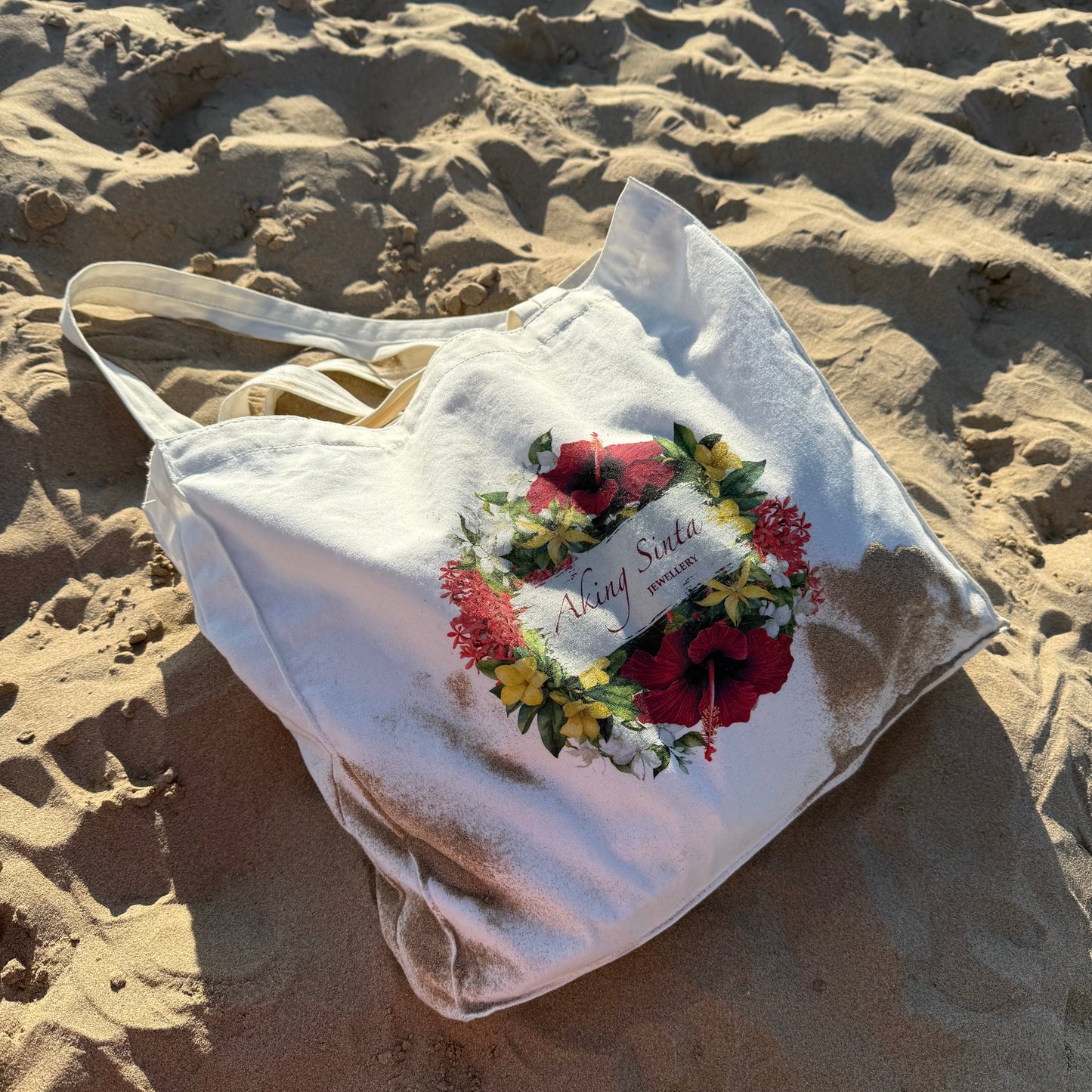 Aking Sinta ‘BET on Yourself’ Floral Tote Bag displayed on white sand beach, featuring Philippine blooms including gumamela, yellow bell, santan, sampaguita, ilang-ilang, with empowering mantra printed