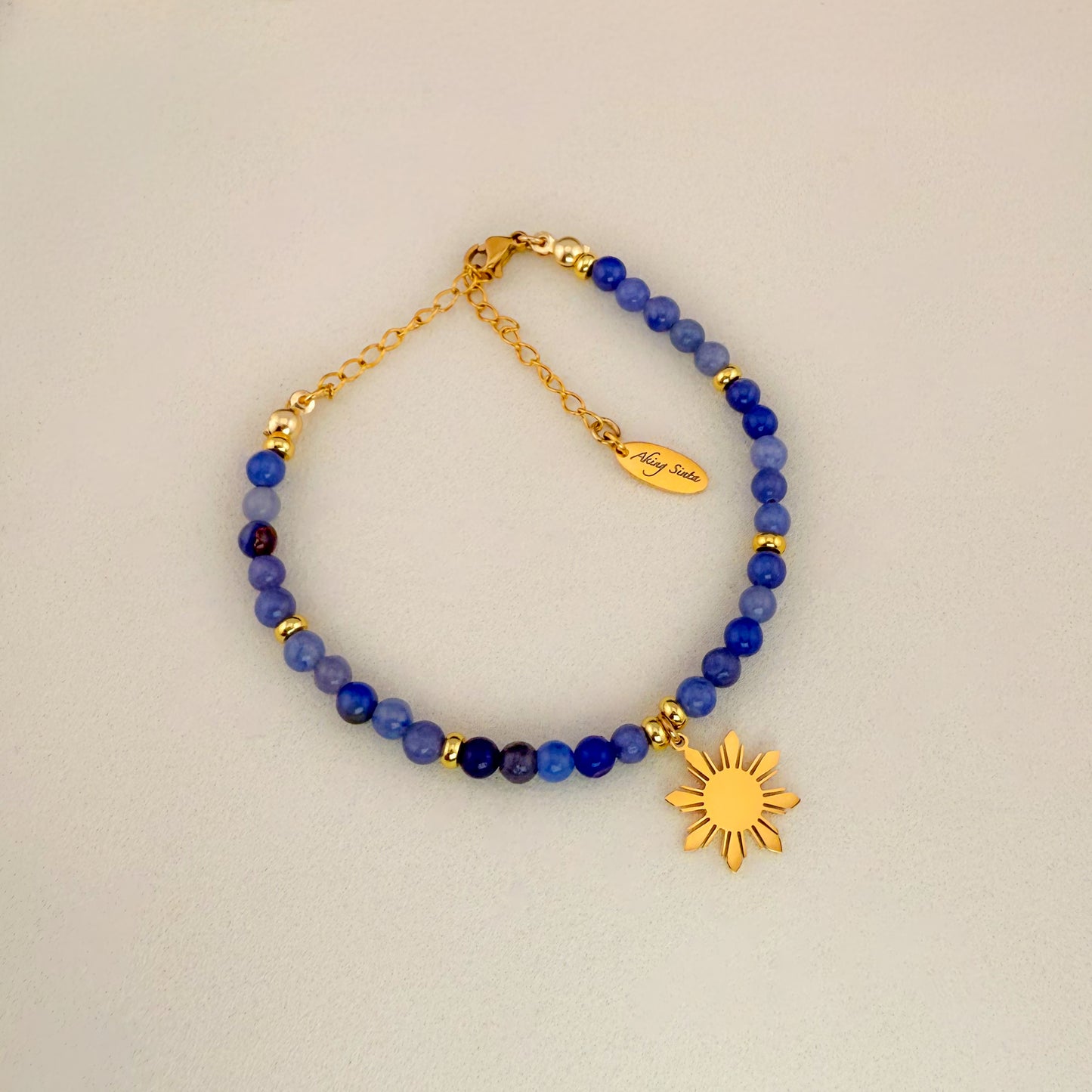 Aking Sinta Blue Aventurine beaded bracelet featuring smooth, misty blue gemstones with a subtle crystalline shimmer, a gold 8-ray Araw sun charm, and a gold extender chain with a teardrop tag engraved with "Aking Sinta."