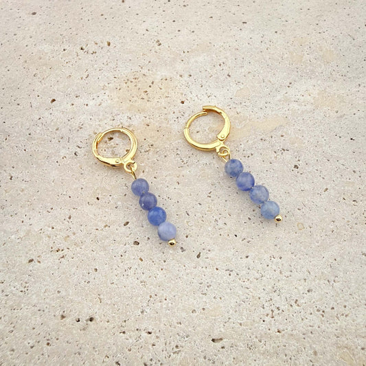 Pair of Aking Sinta gold huggie hoop earrings featuring rectangular Blue Aventurine stone charms on a white marble texture.
