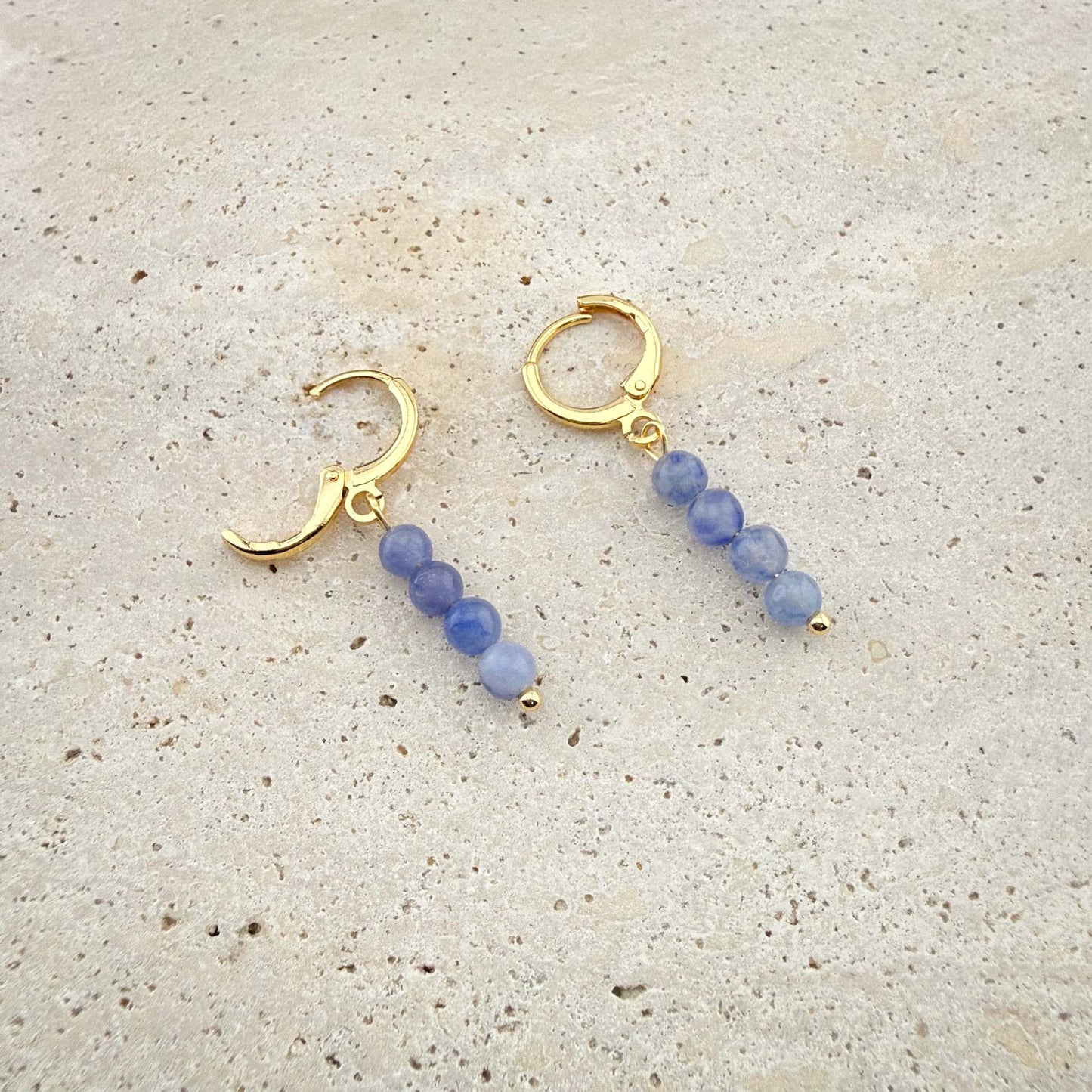 Macro view of Aking Sinta gold Blue Aventurine huggie earrings on marble, with one hinge clasp open to show the secure closure mechanism.