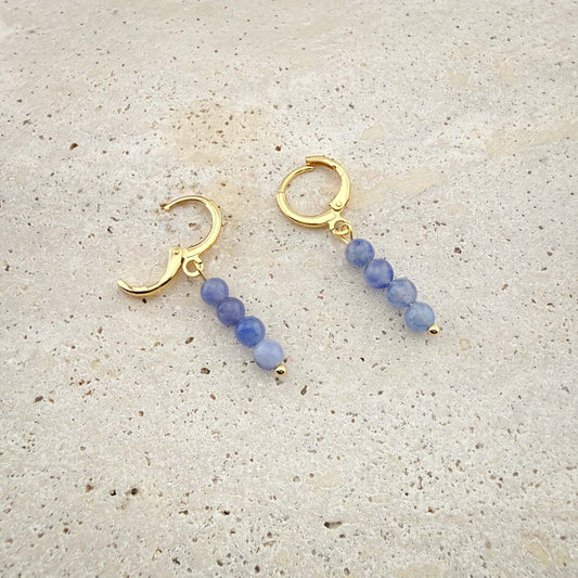 Macro view of Aking Sinta gold Blue Aventurine huggie earrings on marble, with one hinge clasp open to show the secure closure mechanism.