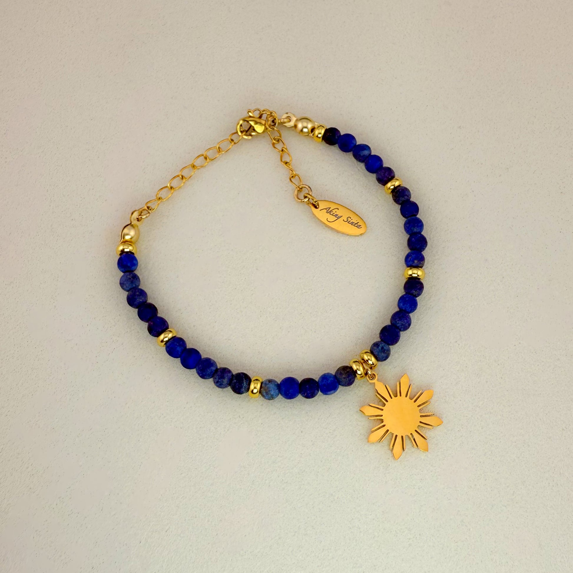 Aking Sinta Blue Tiger Eye beaded bracelet featuring dark, silky navy gemstones with a natural shimmering chatoyancy; accented by a gold 8-ray Araw sun charm and a gold extender chain with an engraved "Aking Sinta" teardrop tag.